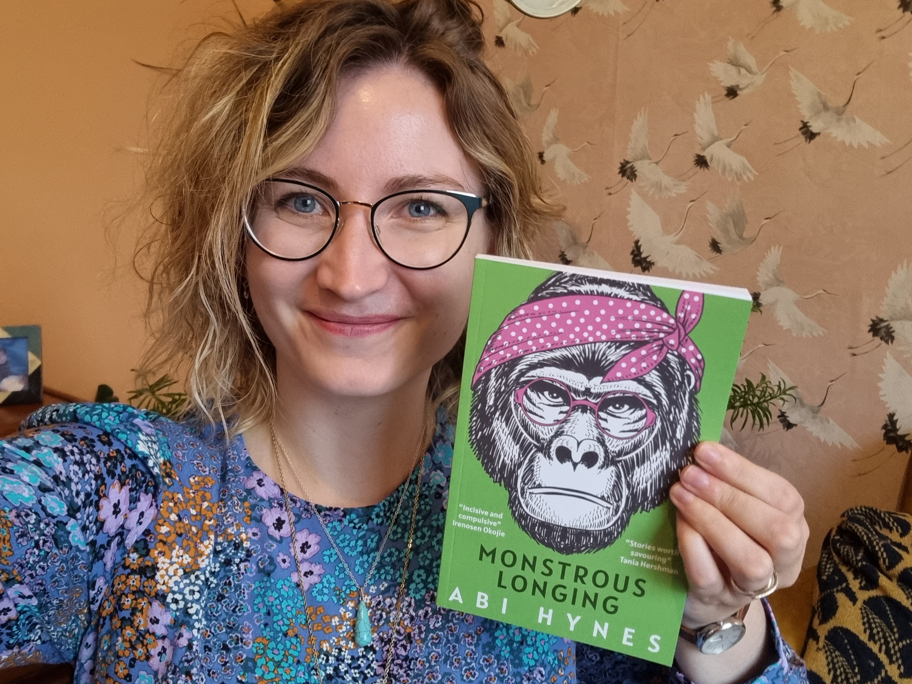 Author Abi Hynes holding up her short story collection Monstrous Longing