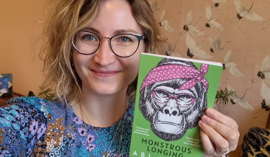 Author Abi Hynes holding up her short story collection Monstrous Longing