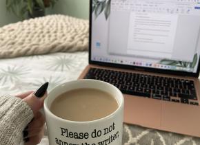 An image of someone holding a mug of coffee in front of an open word document